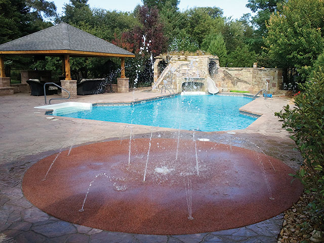 What began as a typical vinyl-liner pool with aluminum coping and a plain concrete deck today has a custom slide, cave, waterfall and tunnel (built in 2005) and is surrounded by an outdoor kitchen, splash pad and other amenities, added in 2010.