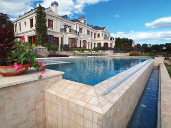 View of pool, catch basin and deck with house in background