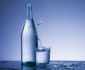 photo of glass of water splashing against a clear glass bottle
