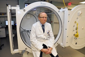 Dr. Paul Harch sits at the mouth of the hyperbaric oxygen chamber in LSU Health.