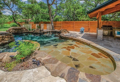 The pool has no steps or tile, but features a number of hardscape details such as the stonework on the beach entry and black pebble finish that work to create an inviting, natural, almost pond-like appearance.