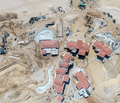 Aerial view of pool and lagoon construction. Note the depots of supplies stacked in the sand, including palm trees and pipe, along with active heavy hydraulic equipment (material handler, backhoe and wheel dozer).