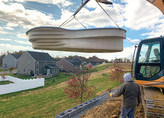 The crew at Bob&rsquo;s Pools creeps toward a waiting hole with a fiberglass pool suspended from a Case excavator with a grappling attachment. The company works with other installers in the area to cut per-unit costs for pool delivery. (Photo courtesy Bob&rsquo;s Pools)