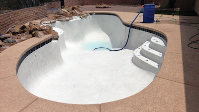 Do not pour undissolved bicarb directly into the pool. A 55-gallon barrel setup like the one shown here can help. With the required amount of bicarb already in the barrel, the hose delivers source water to the barrel's lower inlet. The barrel fills and drains the solution into the pool from the upper outlet. When the pool is full, rinse in any remainder.
