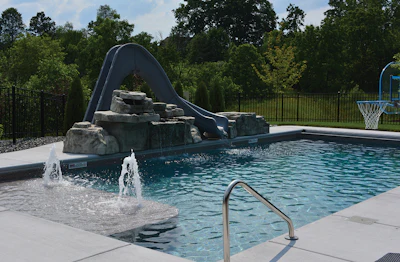 This backyard packs in the fun with a water slide and basketball hoop, while features like the tanning ledge ensure it's just as inviting for relaxation as it is for play.