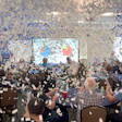 Conference room filled with people celebrating amid falling blue and white confetti