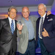 Three senior men in suits posing together at a formal event with purple lighting