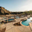 Resort swimming pools nestled against rocky desert mountain landscape with pergola structures