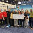 Group of professionals posing with large check at Step Into Swim event booth