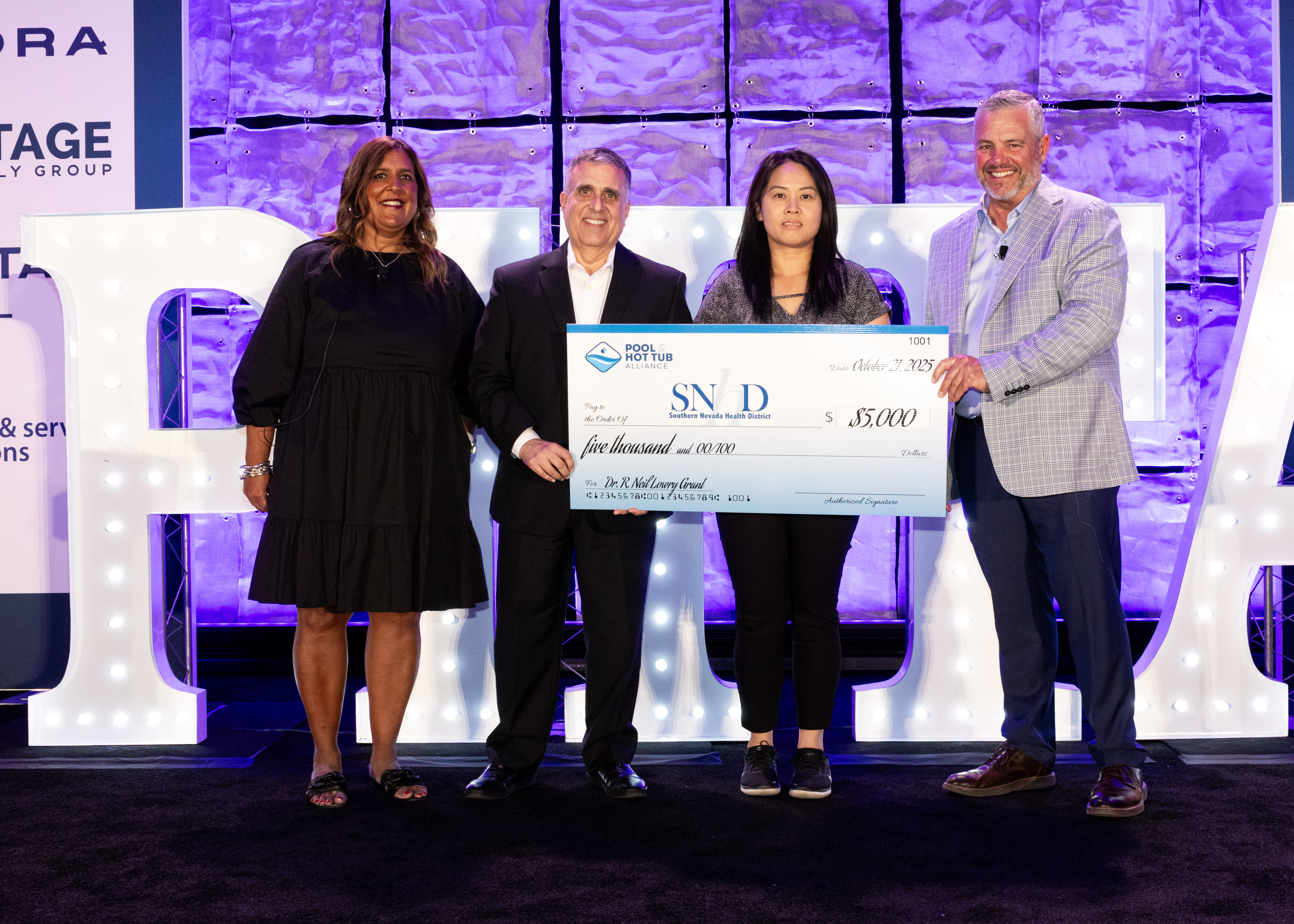Four professionals posing with a large ceremonial check at a corporate event