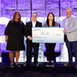 Four professionals posing with a large ceremonial check at a corporate event