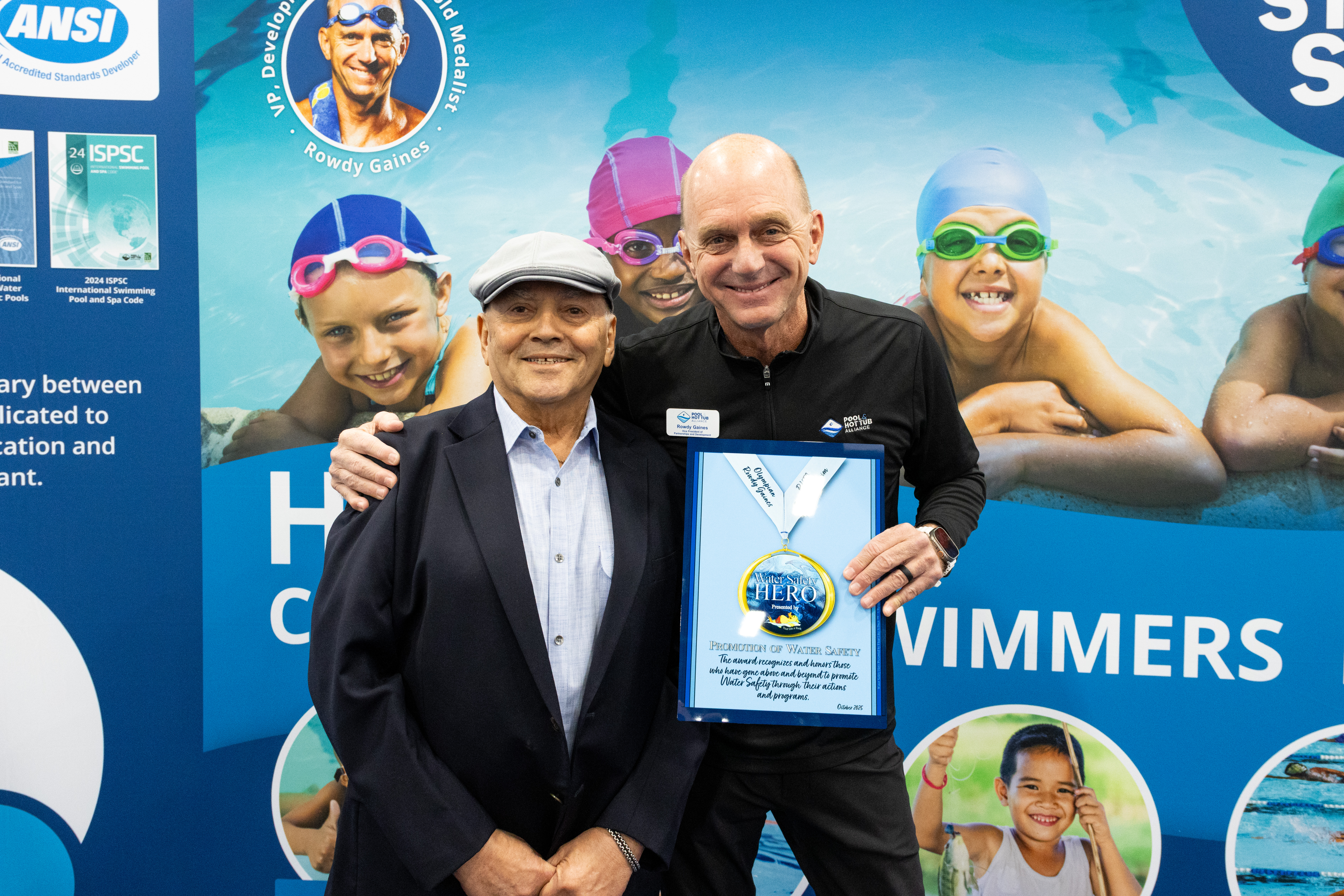 Swimming industry professionals posing with award at conference booth with swimmers in background