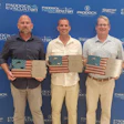 Three men holding American flag wooden awards at a Paddock company awards ceremony in front of branded backdrop