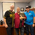 Three men holding a championship trophy in an office, celebrating a sports achievement