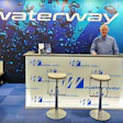 Waterway reception desk with male employee in blue shirt standing at counter with branded backdrop and signage