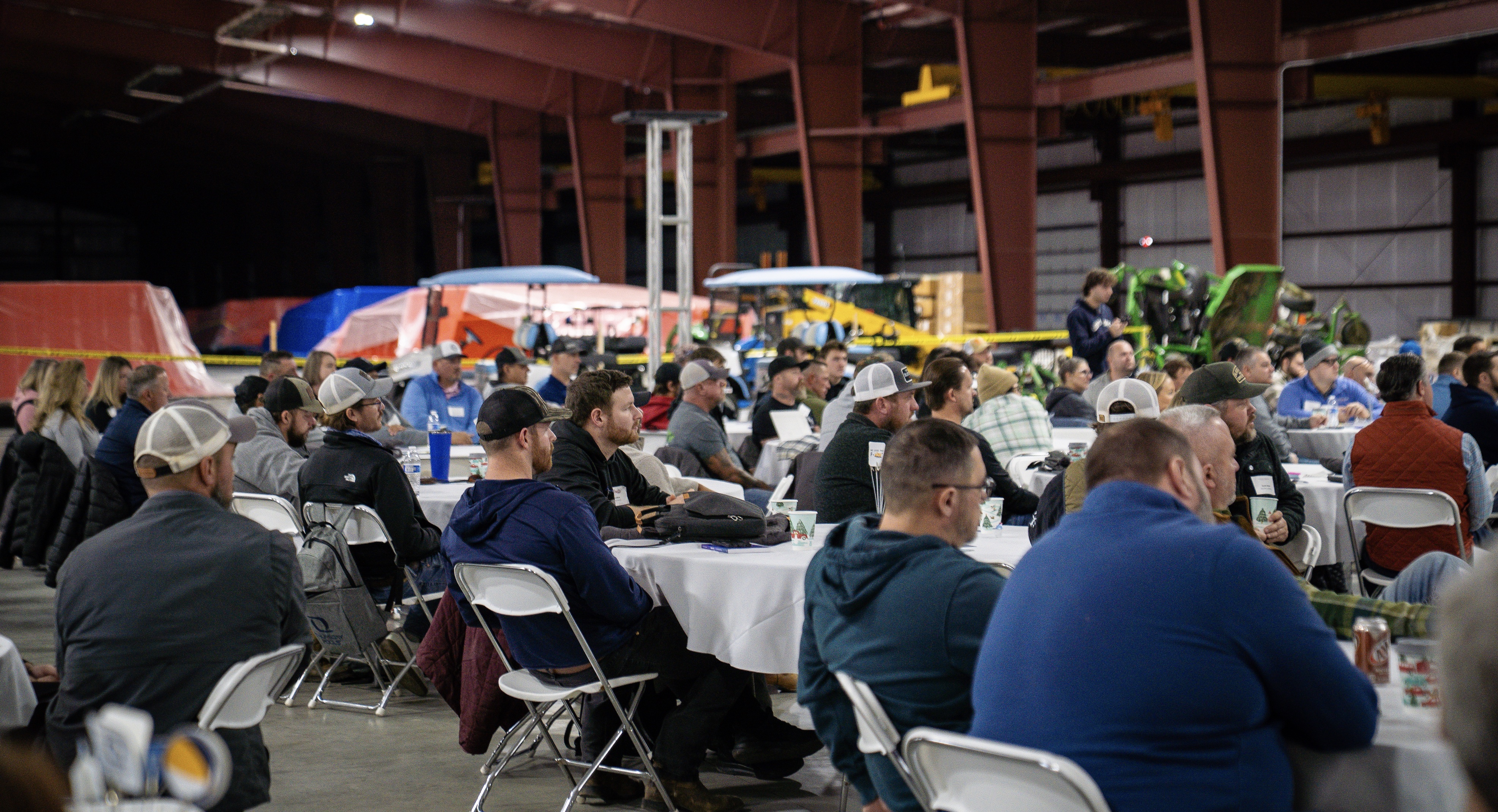 Large indoor community gathering with attendees seated at tables in a warehouse venue during a social event.