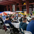 Large indoor community gathering with attendees seated at tables in a warehouse venue during a social event.