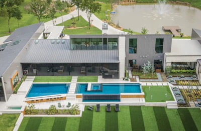 Aerial view of modern home with pool, manicured lawn, and garden landscaping beside water feature