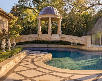 Luxury backyard pool area with domed gazebo, curved stone bridge, and manicured landscaping at golden hour