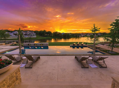 Luxury waterfront home with infinity pool overlooking river at golden sunset with lounge chairs