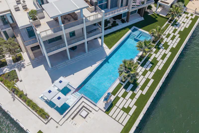 Aerial view of modern luxury waterfront home with pool, manicured lawn, and private dock access