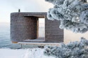 Modern wooden architectural structure with cylindrical tower and open frame overlooking snowy waterfront landscape