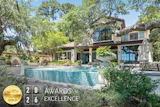 Luxury modern home with turquoise pool surrounded by mature trees and manicured landscaping, featuring 2026 Awards of Excellence gold badge