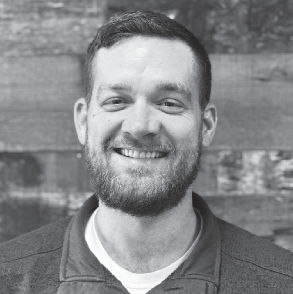 Smiling man with beard in black and white portrait photo against brick wall background Headshot