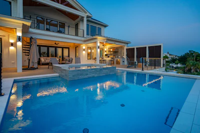 Luxury modern home with illuminated pool and spa at twilight, featuring contemporary architecture and outdoor living space