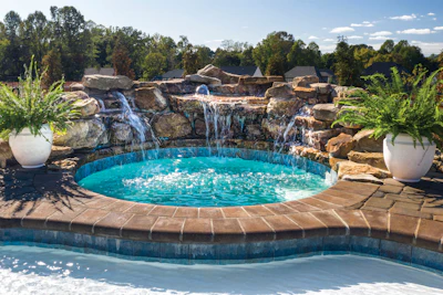 Luxury backyard pool with turquoise water, cascading stone waterfall, and tropical landscaping