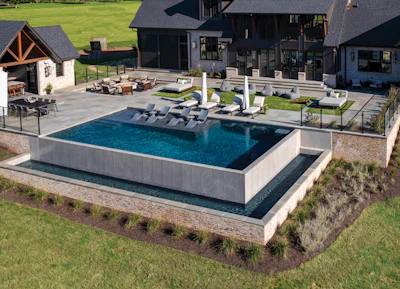 Aerial view of luxury home with modern architecture, rectangular pool, lounge seating, and manicured lawn