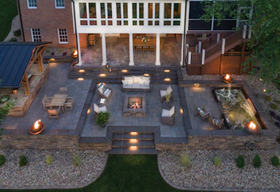 Aerial view of luxury backyard patio with fire pits, seating areas, modern home, and manicured landscaping at dusk