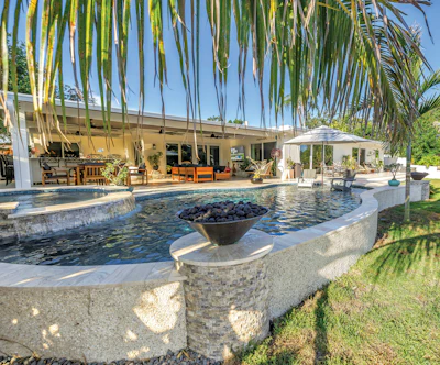 Luxury backyard with resort-style pool, fire pit, and modern home under palm trees