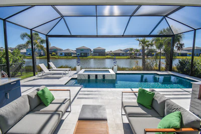Luxury waterfront pool deck with lounge seating, spa, and lake view under screened pavilion
