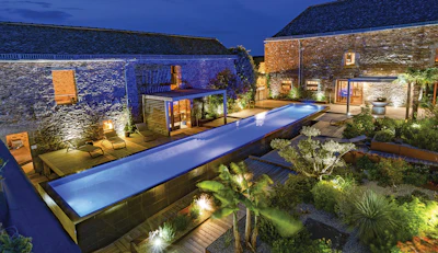 Luxury courtyard home at night with illuminated lap pool, stone buildings, and ambient landscape lighting