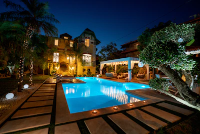 Luxury home at night with illuminated pool, palm trees, and Mediterranean-style architecture
