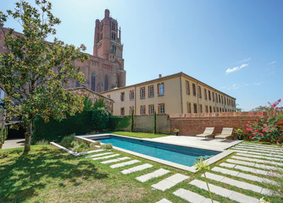 Tuscan villa with ochre facade, infinity pool, manicured gardens, and medieval bell tower backdrop