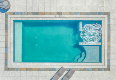 Overhead view of a turquoise swimming pool with a person swimming and lounge chairs on the surrounding deck