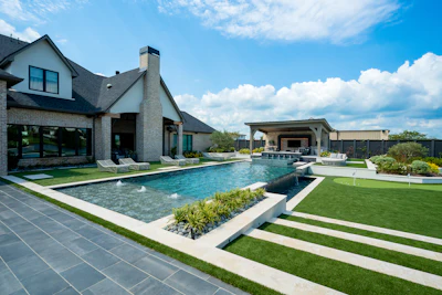Modern luxury home with resort-style pool, manicured lawn, and contemporary architecture under blue sky