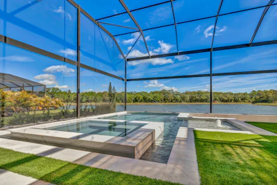 Modern luxury pool and spa overlooking a river with screened enclosure and manicured lawn