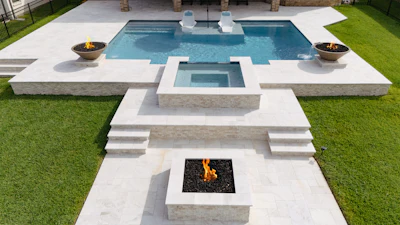 Luxury backyard with rectangular swimming pool, spa, fire pits, and manicured lawn surrounded by white concrete decking