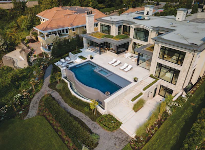 Aerial view of luxury modern home with curved swimming pool, terrace, and manicured grounds