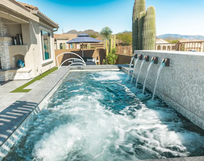 Modern desert home with sparkling swimming pool, tall saguaro cactus, and mountain views under clear blue sky
