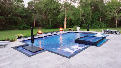 Luxury backyard pool and spa with patio, lounge seating, and mature trees at dusk