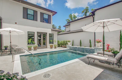 Luxury backyard with rectangular swimming pool, white umbrellas, lounge chairs, and modern home with manicured landscaping