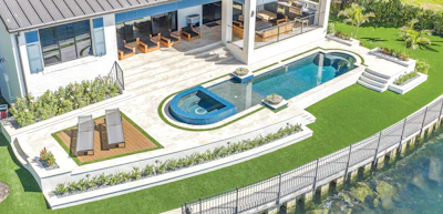 Luxury backyard with rectangular swimming pool, wooden lounge area, modern house with covered patio, manicured lawn, and waterfront views.