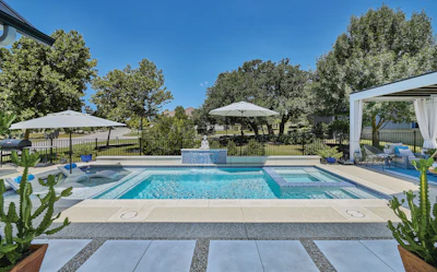 Luxury backyard pool area with white umbrellas, modern pergola, blue water feature, and manicured landscaping with mature trees