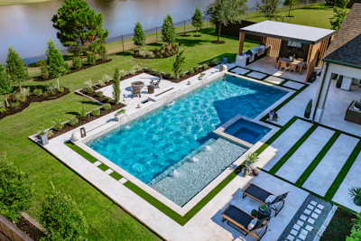 Aerial view of luxury backyard with resort-style swimming pool, spa, lounge area, and manicured landscaping beside a waterfront property