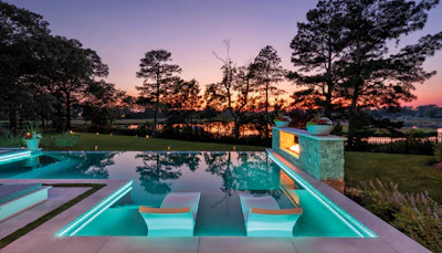 Luxury poolside terrace at sunset with neon turquoise lighting, overlooking a serene lake and tree-lined landscape at dusk.