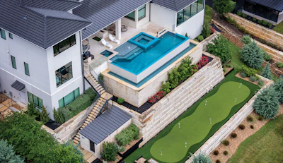 Aerial view of modern luxury home with infinity pool, manicured lawn, mini golf course, and contemporary architecture
